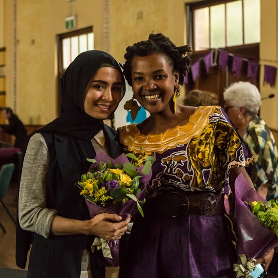 two women holding bouquets of flowers while smiling and looking at the camera